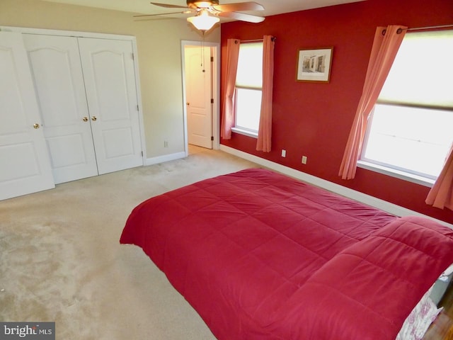 bedroom featuring baseboards, ceiling fan, a closet, and light colored carpet