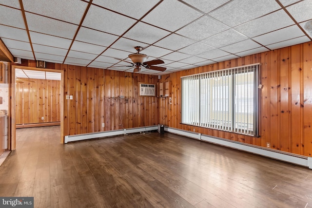 spare room with a ceiling fan, a drop ceiling, wooden walls, hardwood / wood-style flooring, and a baseboard radiator