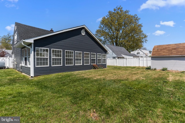 rear view of house with a yard, fence, and roof with shingles