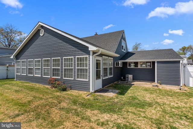 rear view of property featuring fence, a shingled roof, and a yard