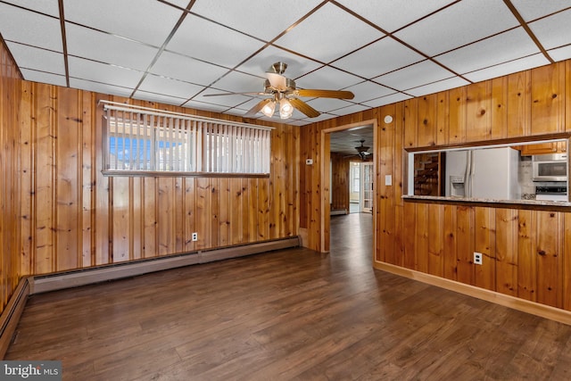 unfurnished room with a ceiling fan, wood walls, baseboard heating, and wood finished floors