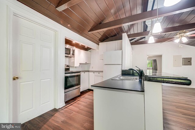 kitchen with dark countertops, appliances with stainless steel finishes, lofted ceiling with beams, a sink, and white cabinetry