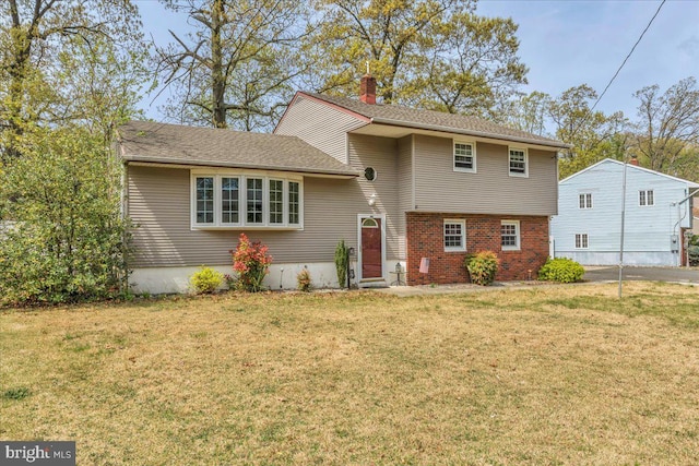 tri-level home with a chimney, brick siding, and a front yard