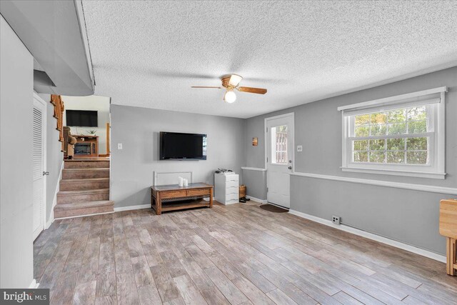 unfurnished living room with a textured ceiling, stairs, a ceiling fan, baseboards, and wood finished floors