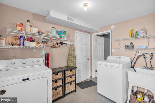 clothes washing area with laundry area, washer and clothes dryer, a sink, and visible vents