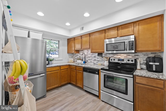 kitchen featuring brown cabinetry, visible vents, a sink, stainless steel appliances, and light wood-style flooring