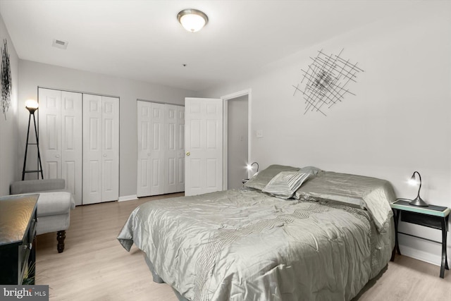 bedroom with light wood-style floors, baseboards, two closets, and visible vents