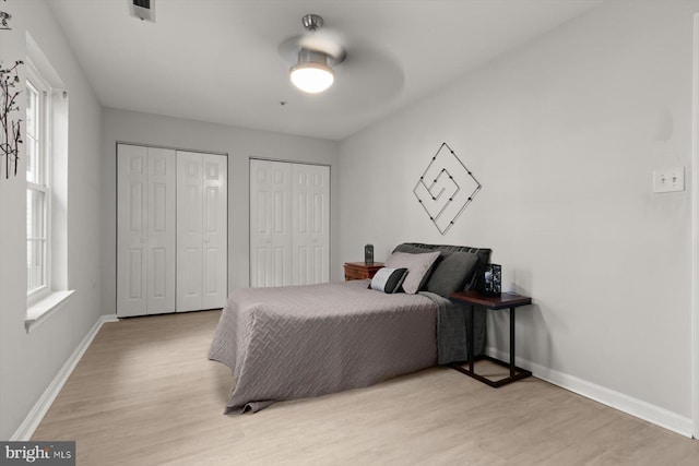 bedroom with a ceiling fan, visible vents, baseboards, multiple closets, and light wood-style flooring