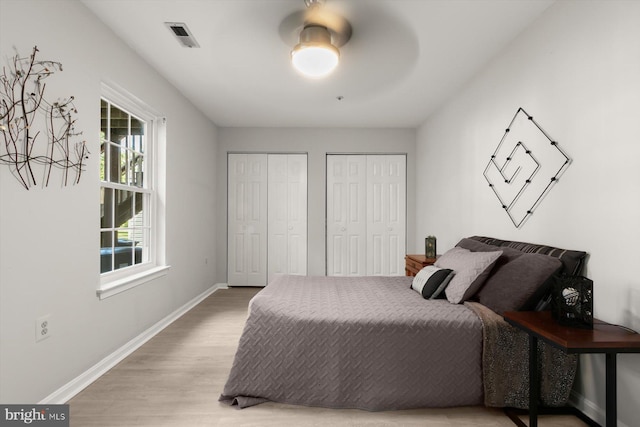 bedroom with baseboards, light wood-style flooring, multiple closets, and a ceiling fan