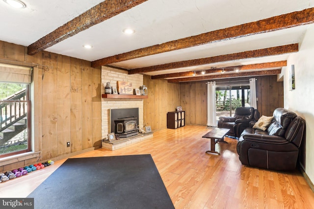 living room featuring a wood stove, wood finished floors, wood walls, and beamed ceiling