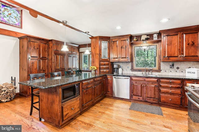 kitchen with a sink, stainless steel appliances, a peninsula, a kitchen bar, and backsplash