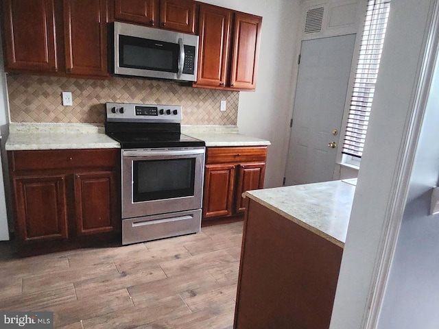 kitchen featuring light wood-style floors, decorative backsplash, appliances with stainless steel finishes, and light countertops