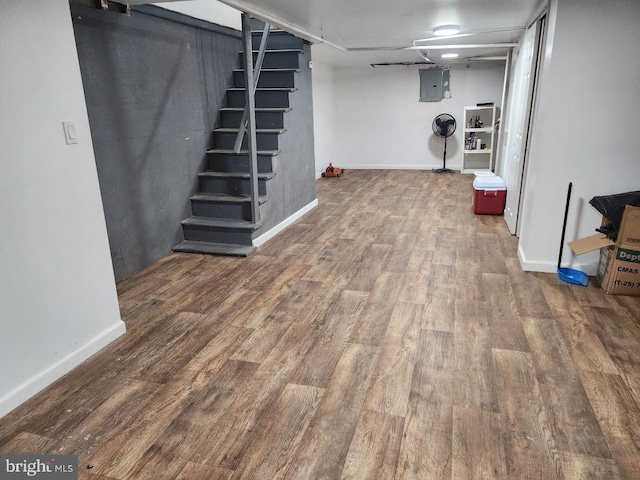 finished basement with baseboards, wood finished floors, electric panel, and stairway