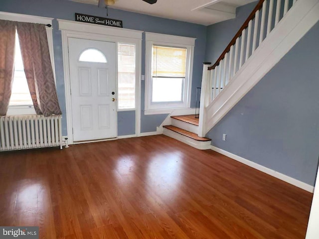 foyer featuring wood finished floors, baseboards, radiator heating unit, and stairway