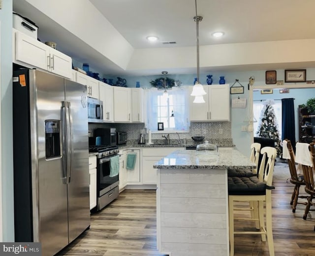 kitchen with appliances with stainless steel finishes, white cabinets, light stone countertops, and wood finished floors