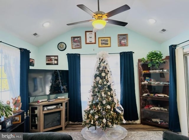 living room with a ceiling fan, vaulted ceiling, wood finished floors, and visible vents