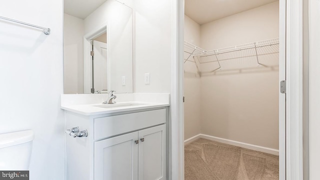 bathroom featuring vanity, toilet, baseboards, and a walk in closet