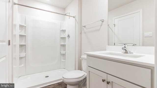 bathroom with wood finished floors, a shower stall, toilet, and vanity