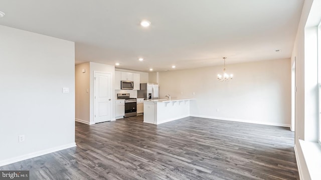 unfurnished living room featuring dark wood-style floors, recessed lighting, a sink, a notable chandelier, and baseboards