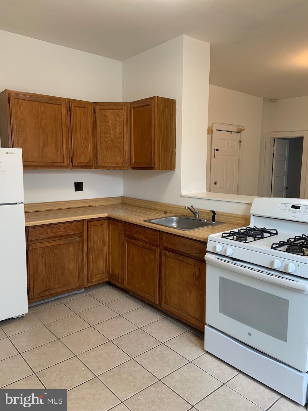 kitchen with white appliances, brown cabinetry, light tile patterned floors, light countertops, and a sink