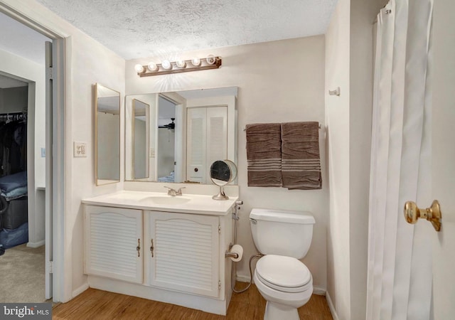 bathroom with a textured ceiling, wood finished floors, vanity, baseboards, and toilet