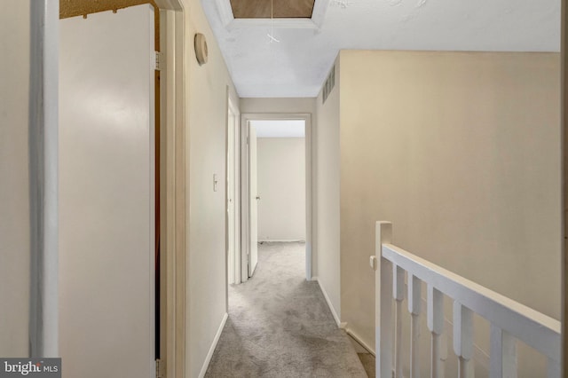 hall featuring visible vents, baseboards, attic access, carpet flooring, and an upstairs landing