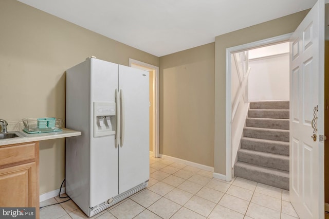 kitchen with a sink, light countertops, white fridge with ice dispenser, baseboards, and light tile patterned floors