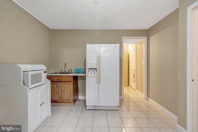kitchen with a sink, white appliances, light countertops, brown cabinetry, and light tile patterned floors