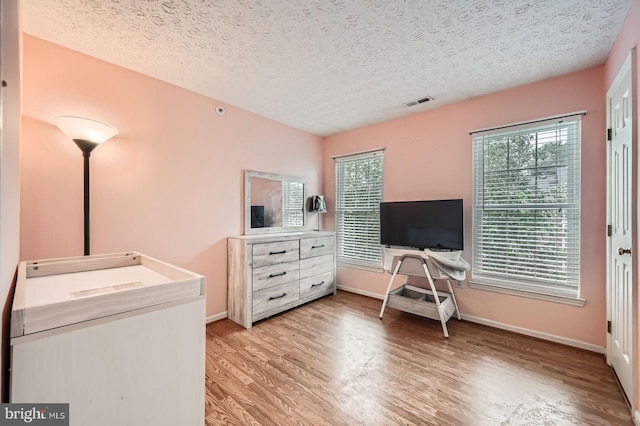 1317 Greenbriar Cir Unit 7-1317, Pikesville, MD 21208 - bedroom with light wood-type flooring, multiple windows, a textured ceiling, and baseboards