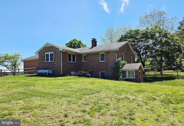 back of property with brick siding, a lawn, and fence