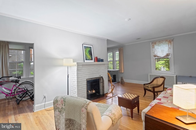 living room featuring radiator, a fireplace, ornamental molding, baseboards, and wood finished floors