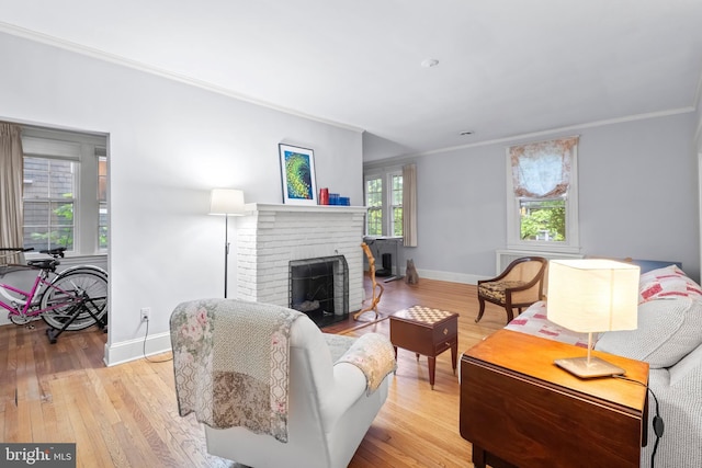 living room with crown molding, baseboards, wood finished floors, and a brick fireplace