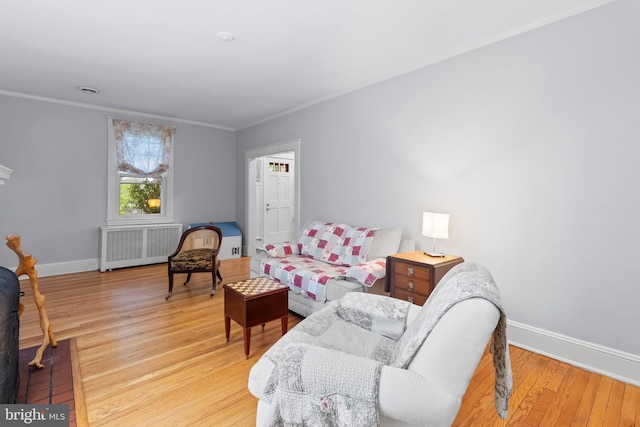 sitting room with radiator heating unit, light wood-type flooring, baseboards, and crown molding