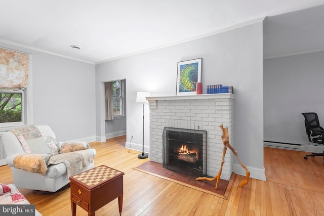 living area featuring a baseboard radiator, a brick fireplace, ornamental molding, hardwood / wood-style flooring, and baseboards