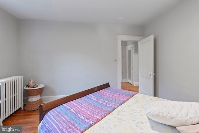 bedroom with radiator heating unit, wood finished floors, and baseboards