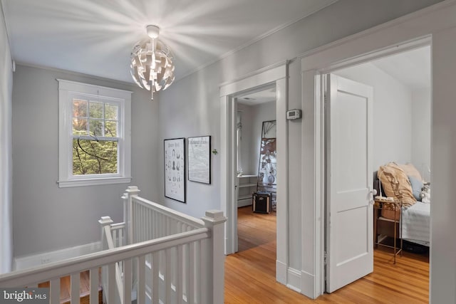 hall with an upstairs landing, a chandelier, light wood finished floors, and crown molding