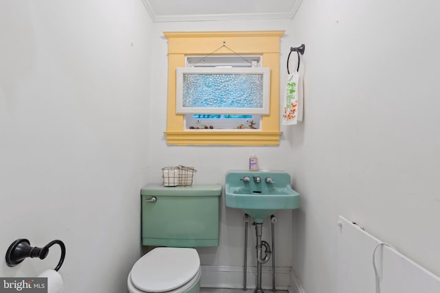 half bathroom featuring toilet, ornamental molding, baseboards, and a sink