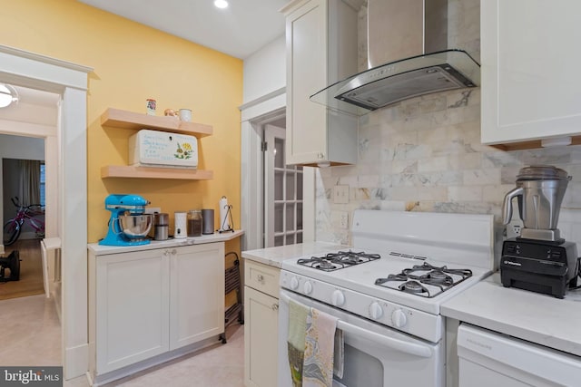 kitchen with white appliances, wall chimney exhaust hood, tasteful backsplash, light countertops, and white cabinets