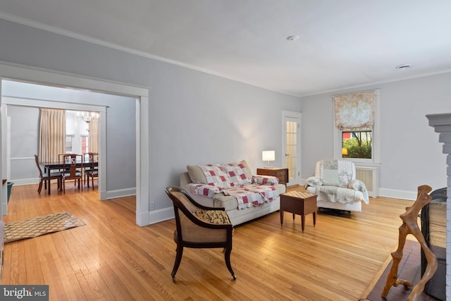 living room with a chandelier, light wood-style floors, ornamental molding, baseboards, and a fireplace