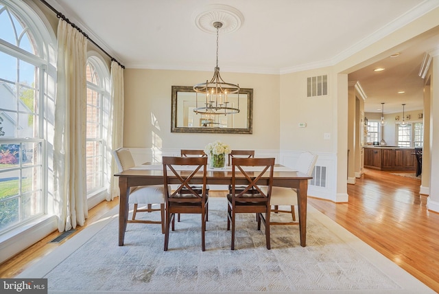 dining area with visible vents, ornamental molding, wainscoting, light wood finished floors, and a notable chandelier