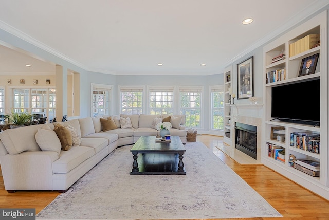 living room featuring crown molding, a fireplace with flush hearth, built in shelves, and light wood-style flooring
