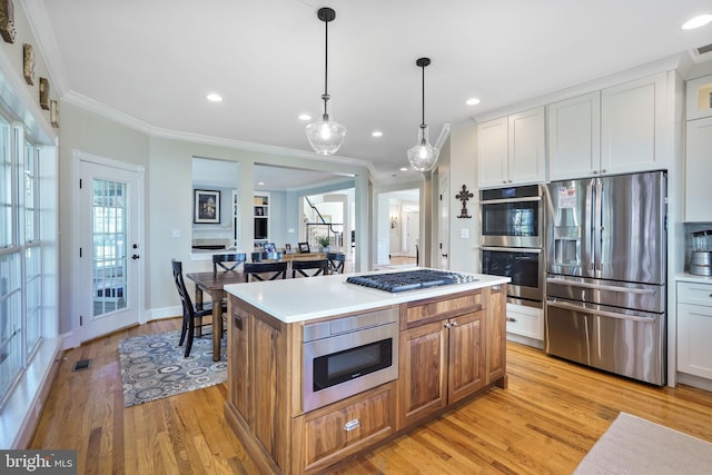 kitchen with crown molding, appliances with stainless steel finishes, light wood finished floors, recessed lighting, and a kitchen island