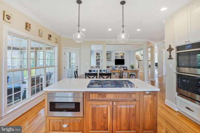 kitchen with a kitchen island, crown molding, appliances with stainless steel finishes, light countertops, and light wood-style floors