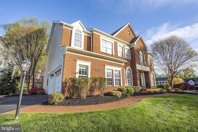 view of front of house with brick siding, an attached garage, aphalt driveway, and a front lawn
