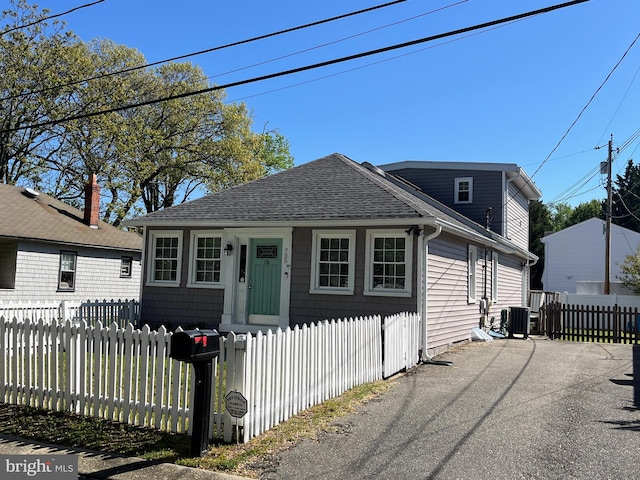 bungalow with roof with shingles, a fenced front yard, and cooling unit