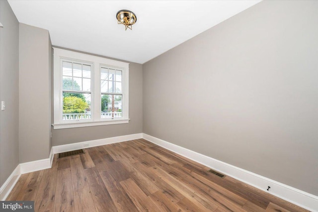 unfurnished room featuring baseboards, visible vents, and wood finished floors