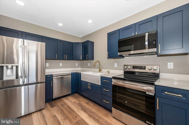 kitchen featuring a sink, light countertops, blue cabinets, light wood finished floors, and appliances with stainless steel finishes
