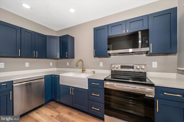 kitchen featuring appliances with stainless steel finishes, light wood-type flooring, a sink, and blue cabinets