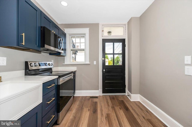 kitchen with appliances with stainless steel finishes, light countertops, baseboards, dark wood-type flooring, and blue cabinets