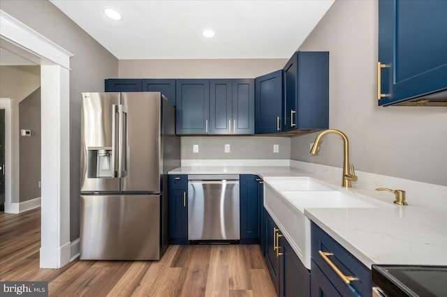 kitchen featuring recessed lighting, light stone counters, blue cabinets, light wood finished floors, and appliances with stainless steel finishes